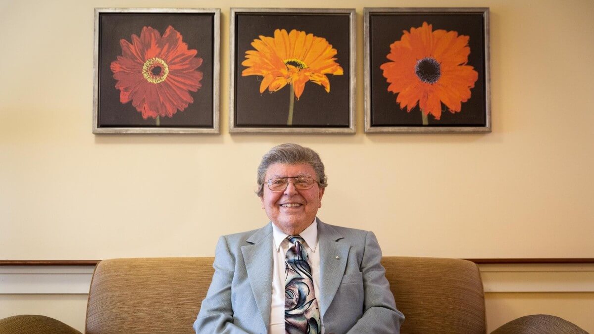 Older man sitting in front of flower paintings