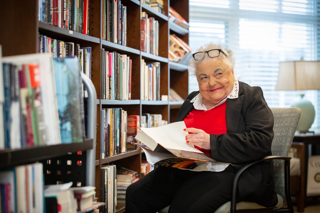 a woman sitting with a book in front of a bookshelf