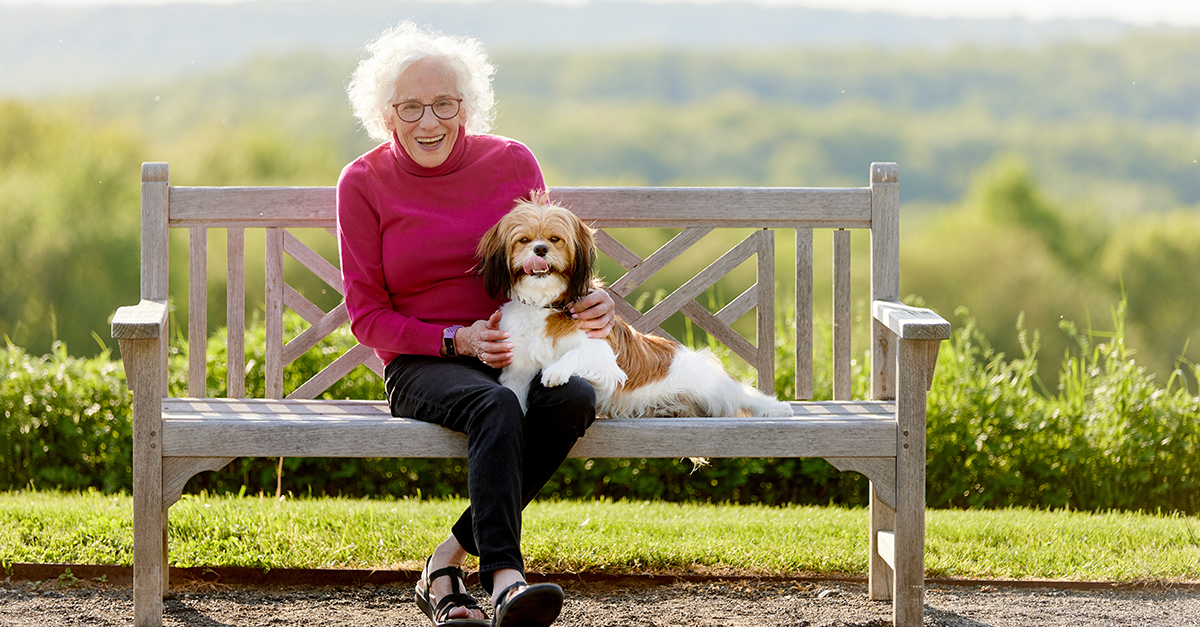 an older woman sitting on a bench with her dog, smiling