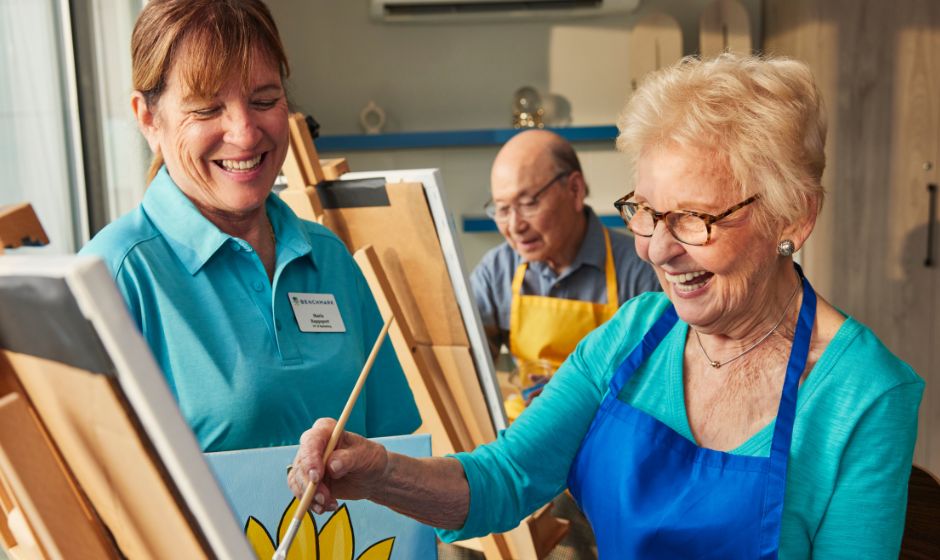 a senior painting with an associate watching and smiling